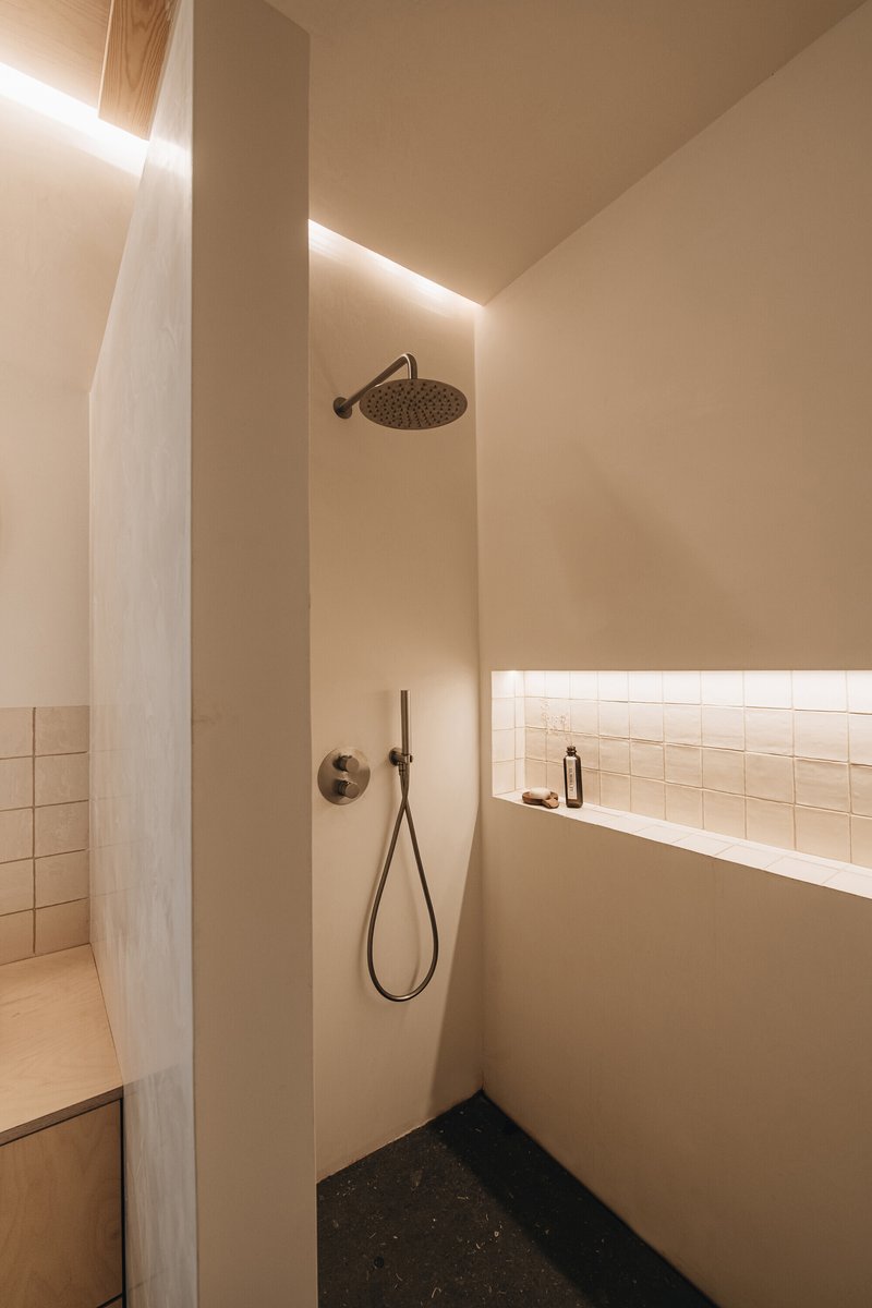 Shower corner with overhead rain fixture, polished plaster walls and concealed linear lighting at the ceiling