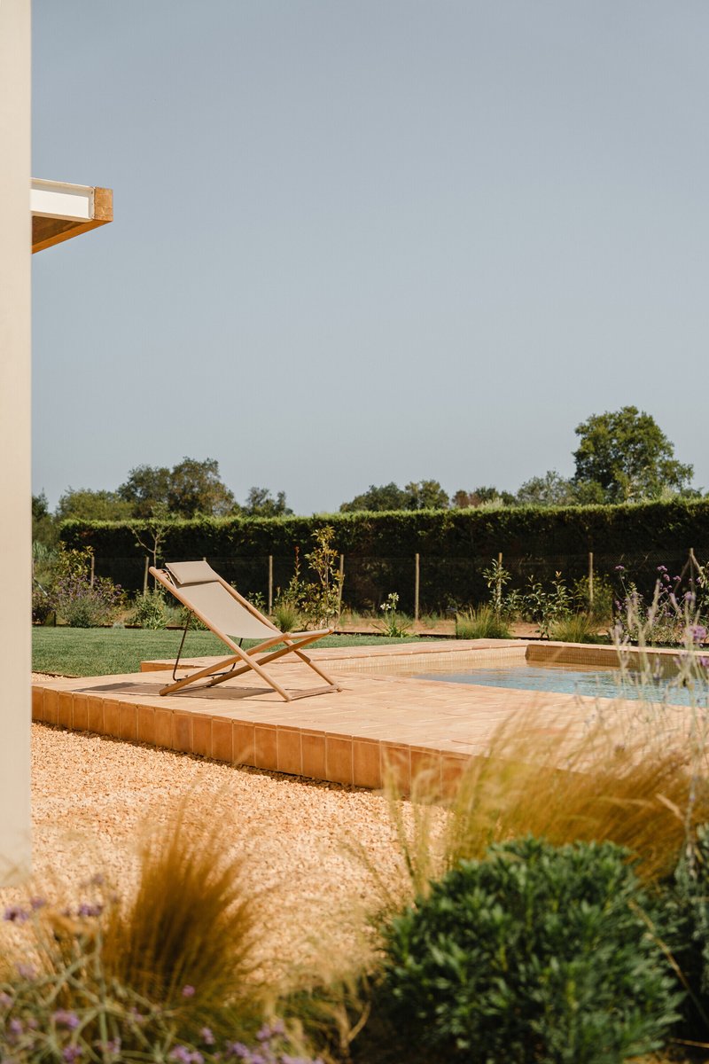 Timber deck terrace with canvas lounge chair beside gravel garden and hedgerow