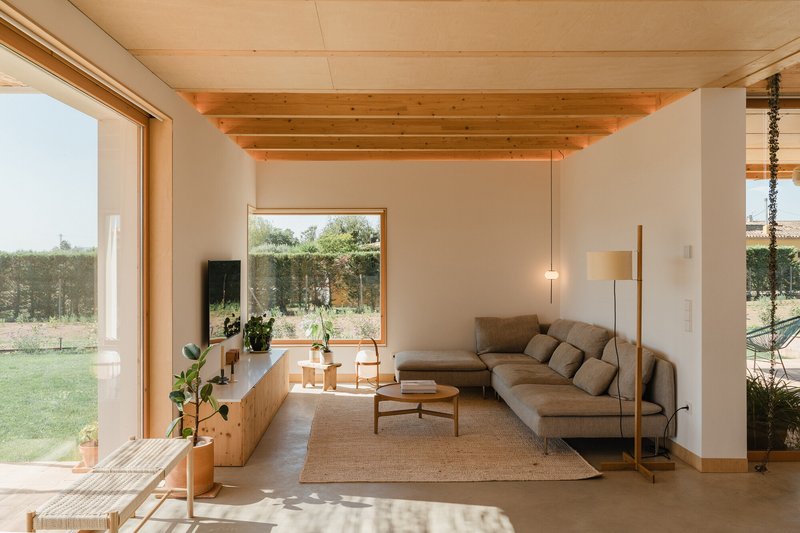 Living room with exposed timber ceiling beams and large window framing views of the grassy lawn beyond