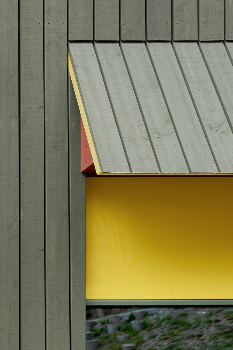 Detail of a triangular window canopy with red underside against green vertical timber cladding