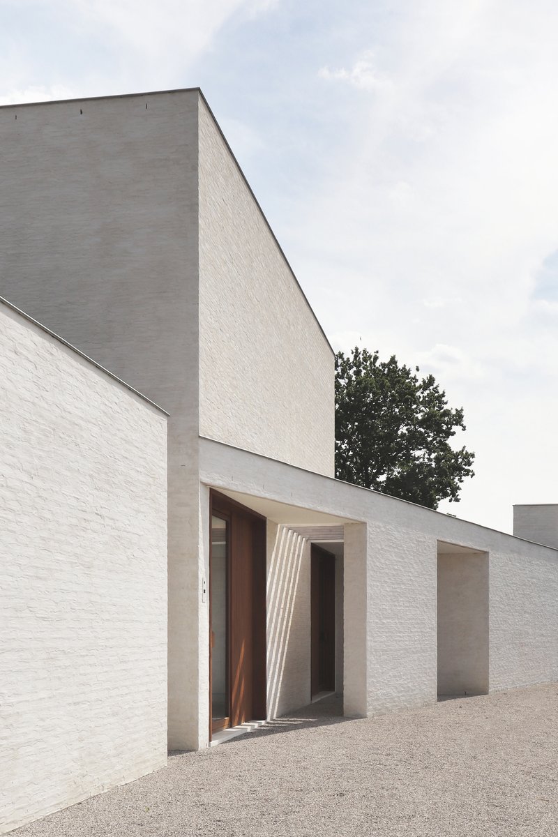 Entrance with ribbed concrete canopy framing a timber door set in white brick walls beneath an overcast sky