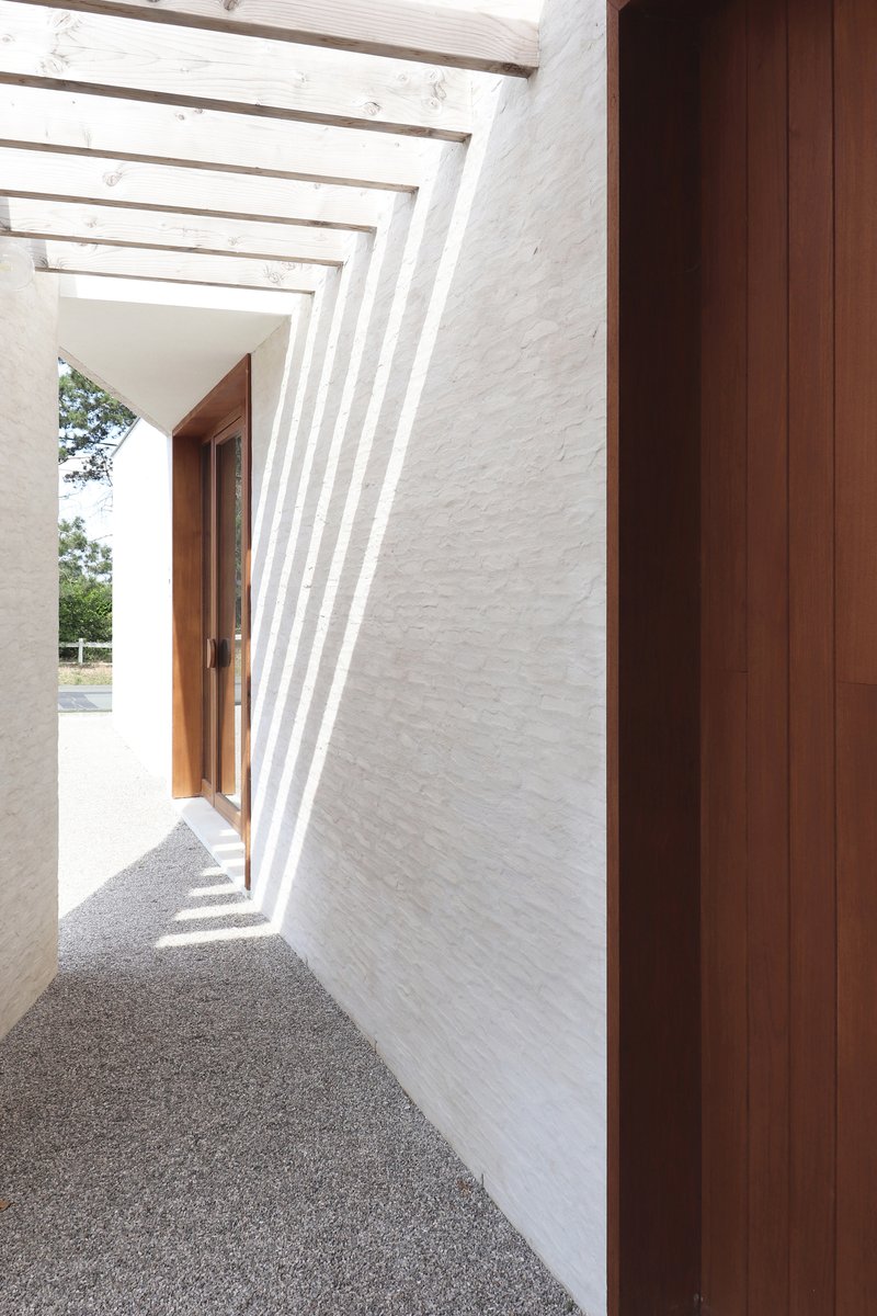 View through the angled concrete ribs of the entry canopy casting shadows on the white brick wall