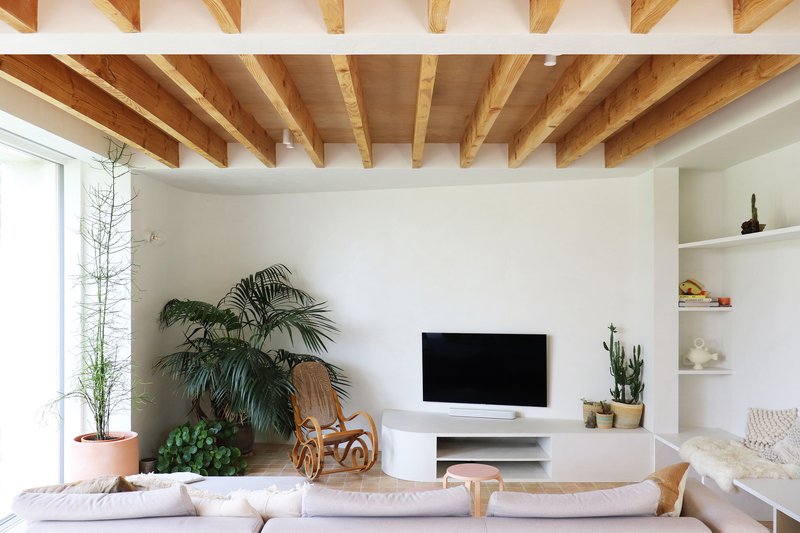 Living room with exposed timber joists and beams over white walls and potted plants near a window