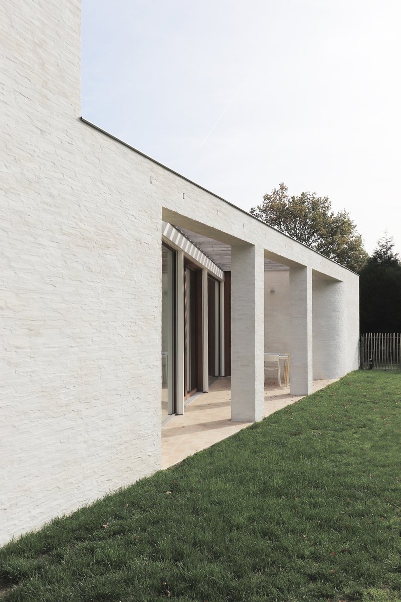 Recessed porch with concrete columns and deep overhang set into white brick facade