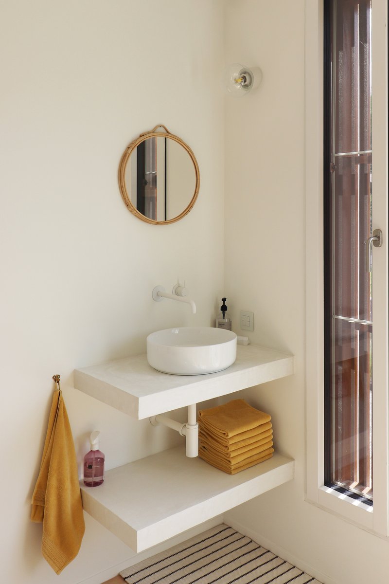 Bathroom vanity with floating shelves, round vessel sink, circular mirror and tall louvered wooden door