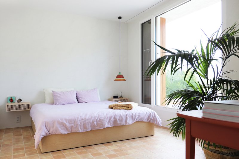 Bedroom with terra-cotta tile floor and full-height glazing framed by potted palm fronds