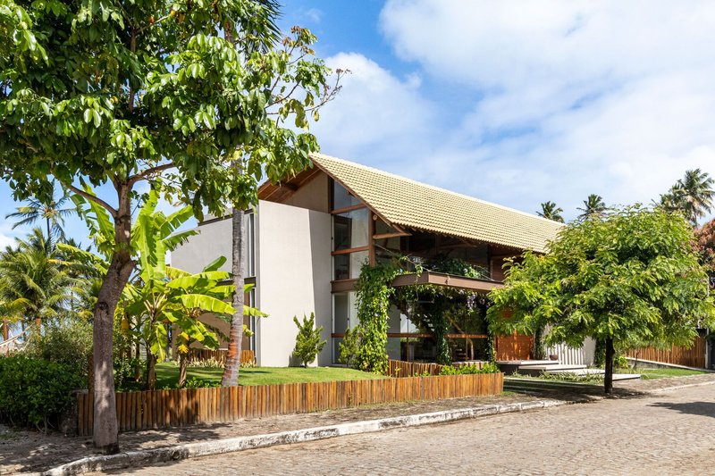 Street view of the gabled tile roof rising above a vertical timber fence and tropical planting
