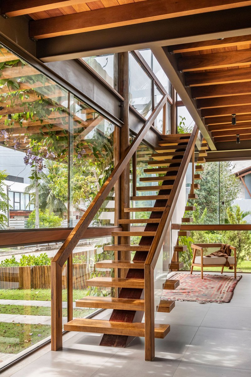 Open-tread timber staircase with diagonal structural bracing and glazed wall revealing the garden beyond