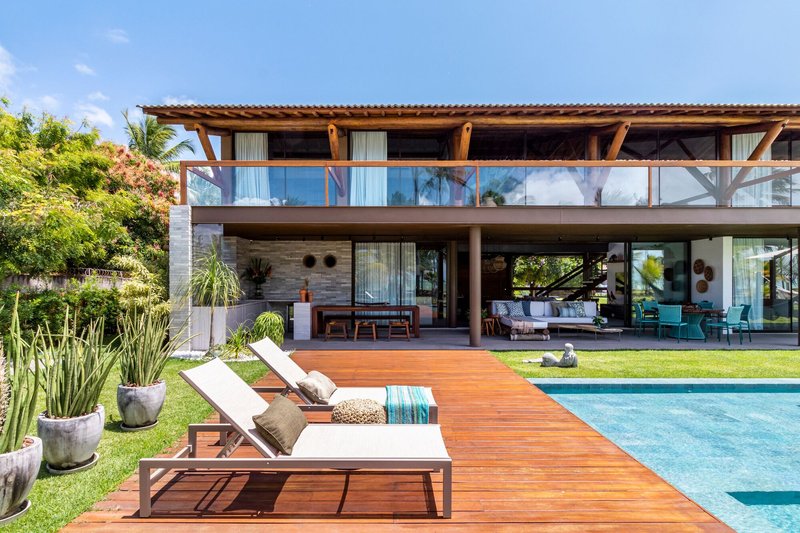 Rear elevation showing timber deck extending from open living area toward swimming pool under clear sky