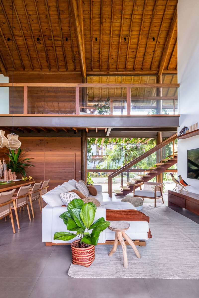 Double-height living space with exposed timber ceiling, mezzanine bridge and open staircase framed by garden views