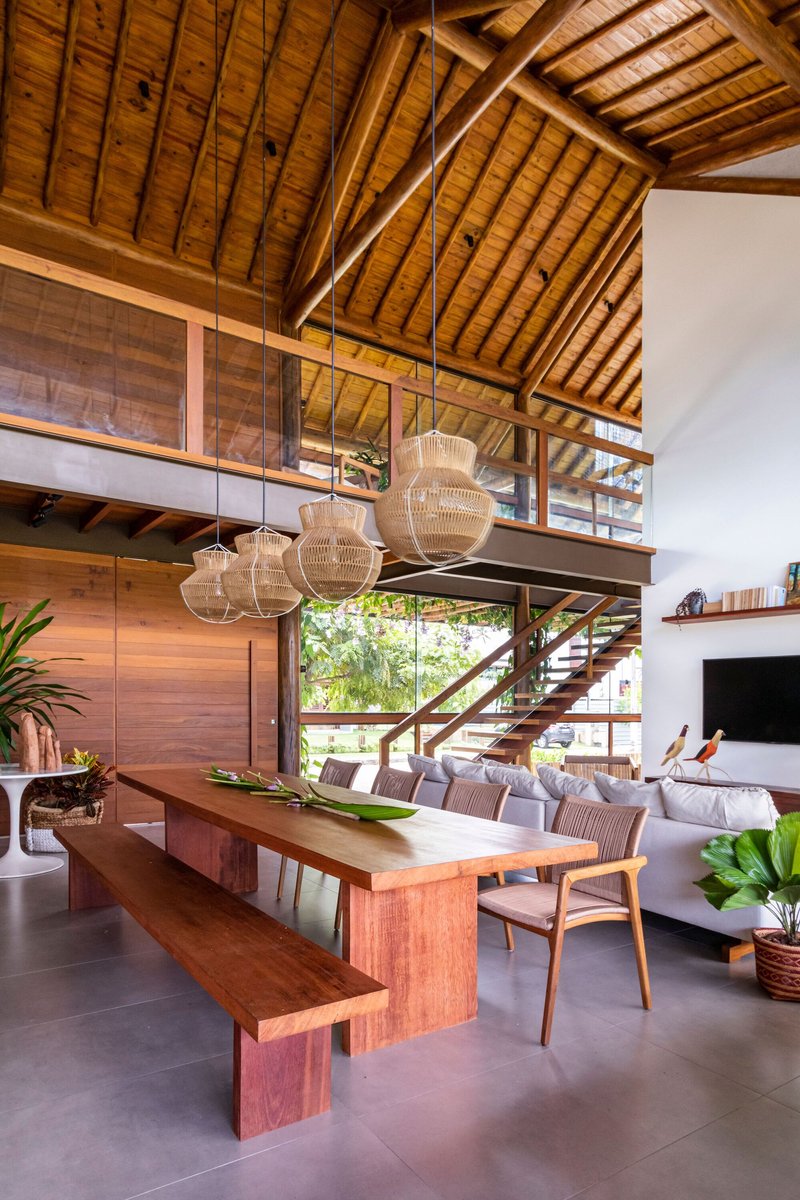 Timber dining table and bench beneath woven pendant lights with mezzanine and pitched ceiling above