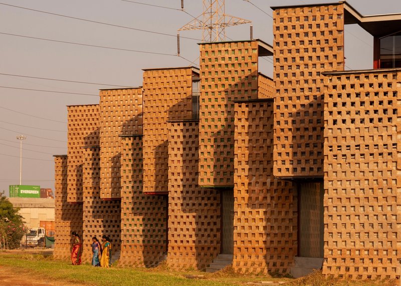 Oblique view of the stepped brick facade with transmission towers visible beyond at golden hour