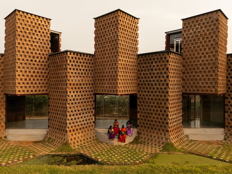 Symmetrical facade of perforated brick columns with glass entrances and visitors in shadow beneath curved canopy