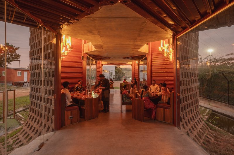 Covered dining area with exposed timber ceiling and perforated brick screen walls at dusk