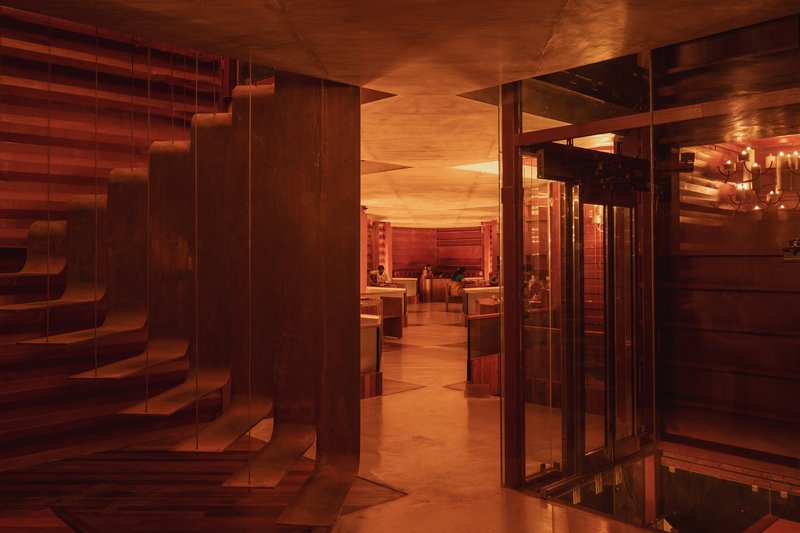 Interior passage with suspended timber staircase and layered timber ceiling panels in warm artificial light