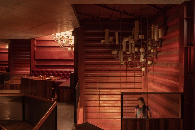 Restaurant interior with tufted leather booth, horizontal timber slat wall, and candle chandelier above