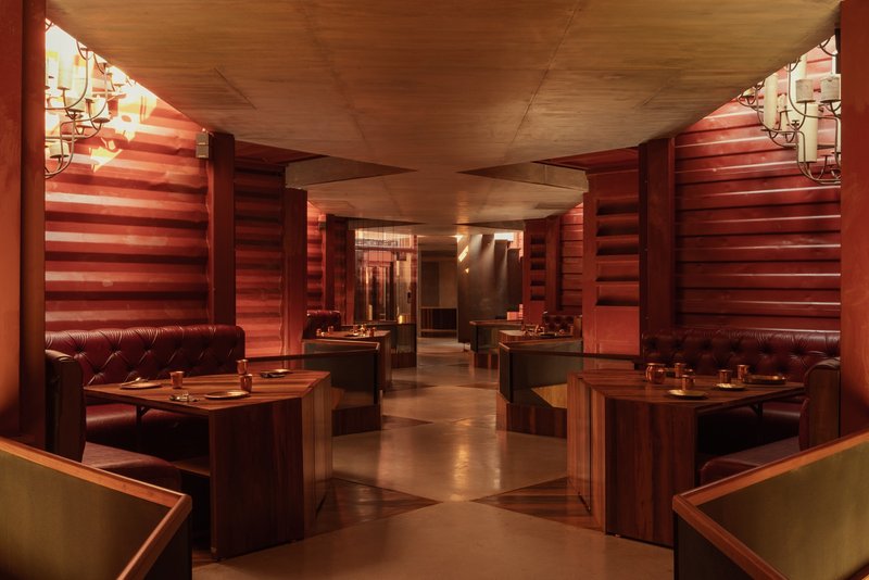 Dining room with angled ceiling plane, horizontal timber cladding, and booth seating under warm lighting