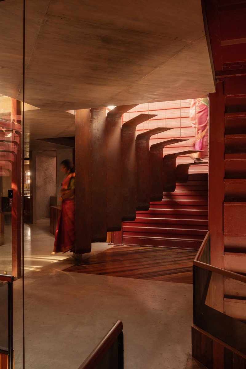 Curved sculptural staircase with horizontal timber slat walls and person descending in traditional dress