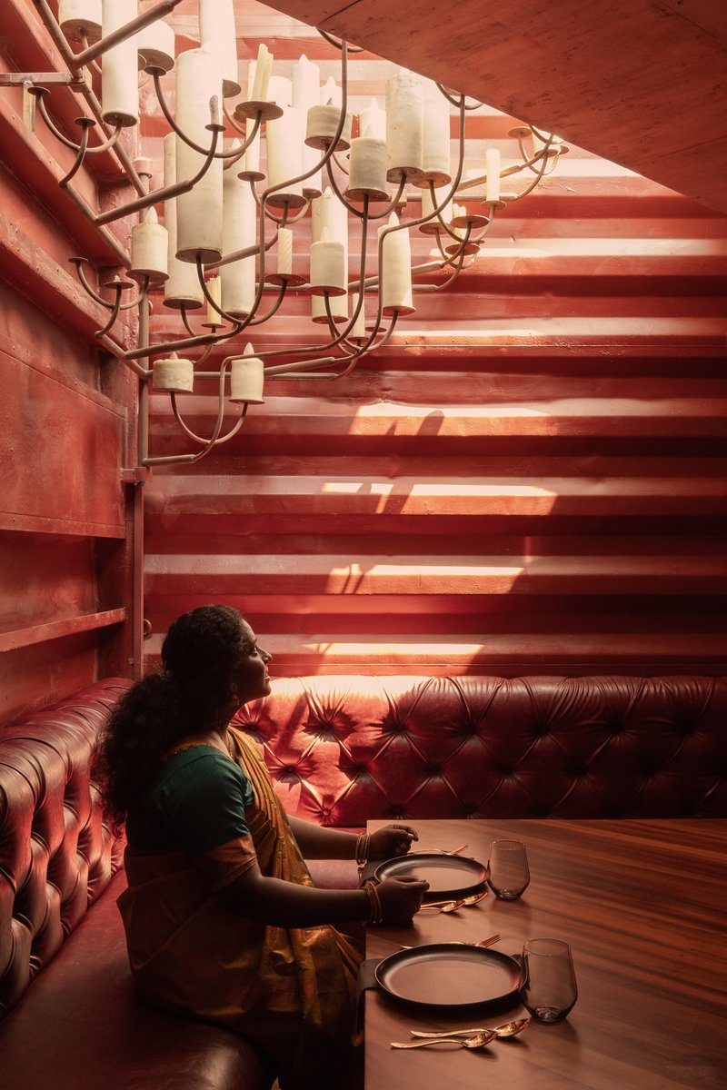 Tufted leather banquette beneath candle chandelier and horizontal timber wall with filtered sunlight