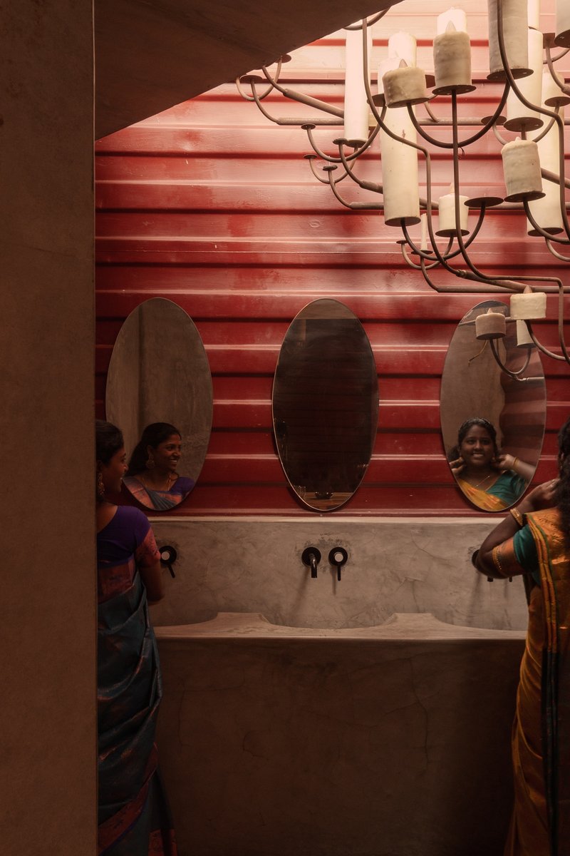 Washroom vanity with oval mirrors, candle chandelier, and horizontal timber slat wall with reflected figures