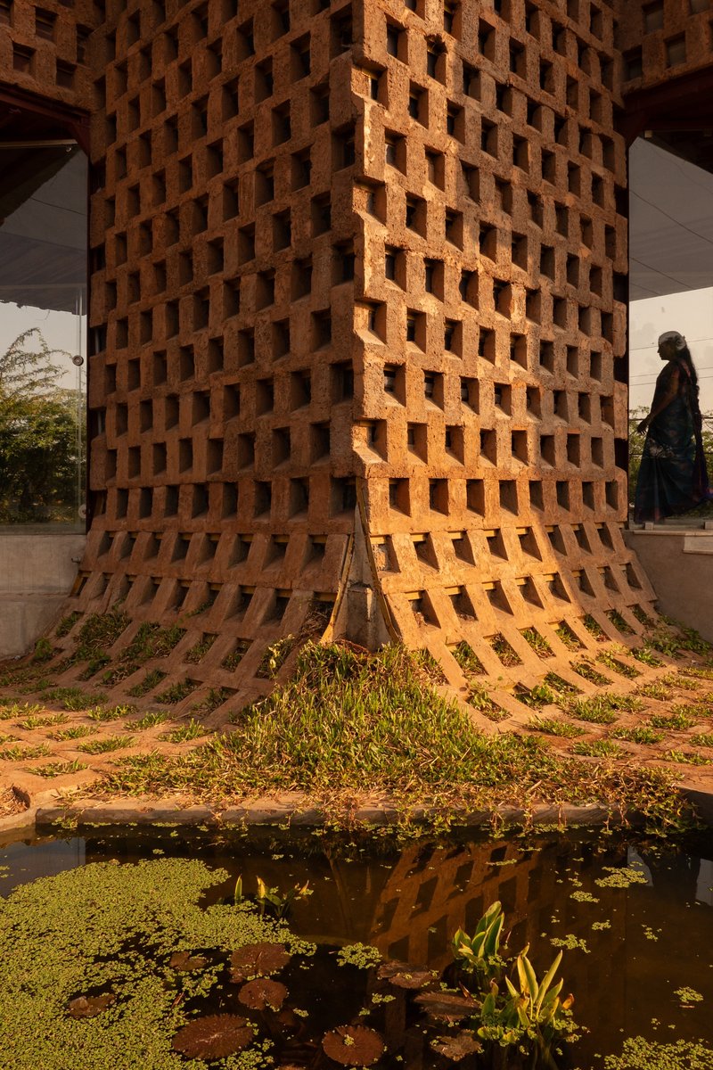 Perforated brick tower with base reflecting in shallow pool edged with water plants and grasses