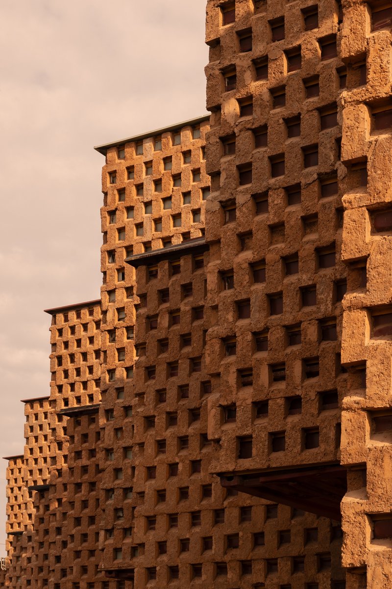 Close-up of the perforated terracotta brick facade with interlocking volumes under warm afternoon light