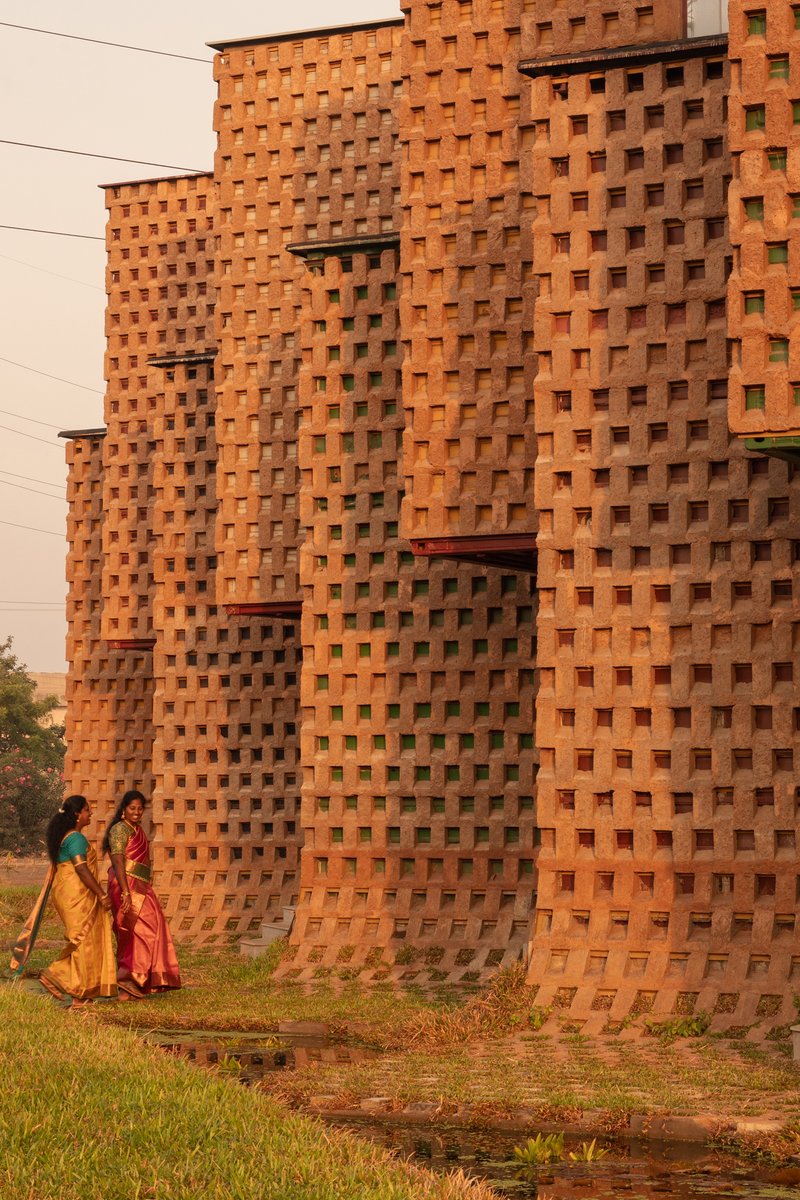 Perforated terracotta brick wall with two figures in traditional dress walking on adjacent grass