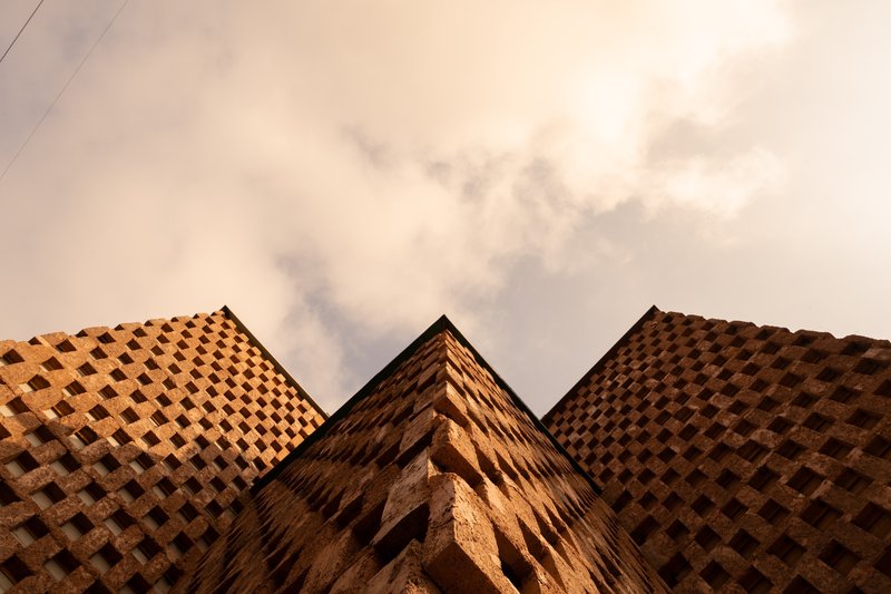 Upward view of the three pyramidal terracotta brick volumes meeting against an overcast sky