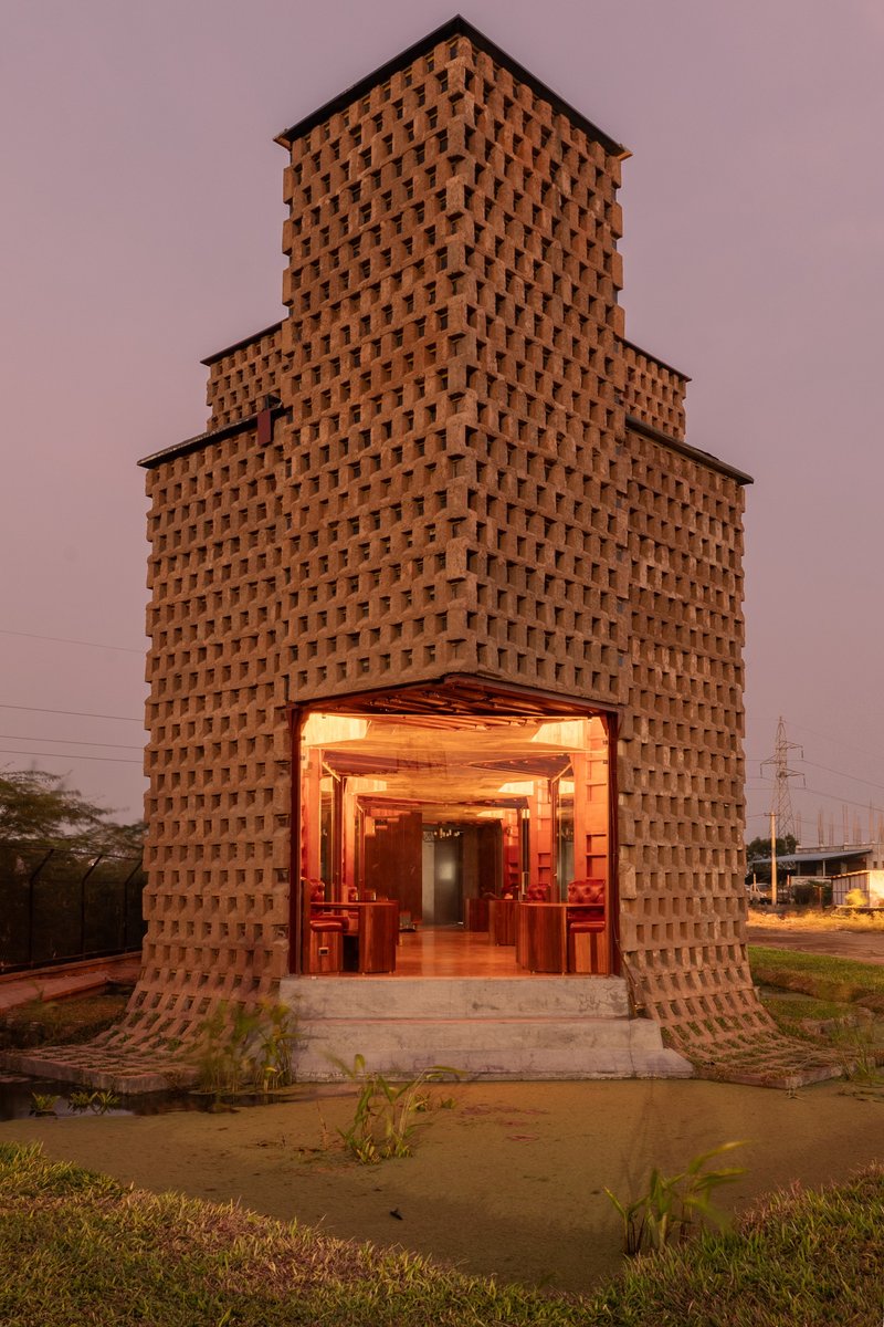 Stepped terracotta brick tower with illuminated arched entrance at dusk under a pink sky