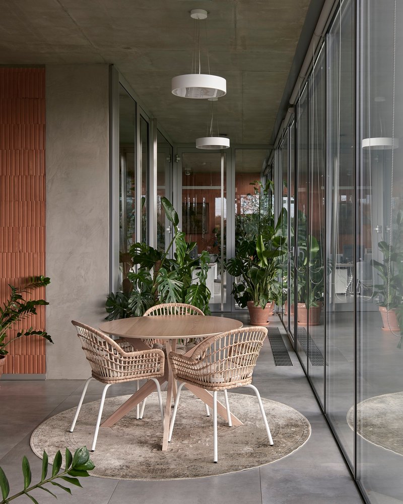 Covered terrace with rattan dining set and potted plants flanked by floor-to-ceiling glazing and timber slat wall