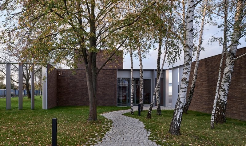 Cobblestone pathway leading through birch trees toward a courtyard entrance between brick volumes