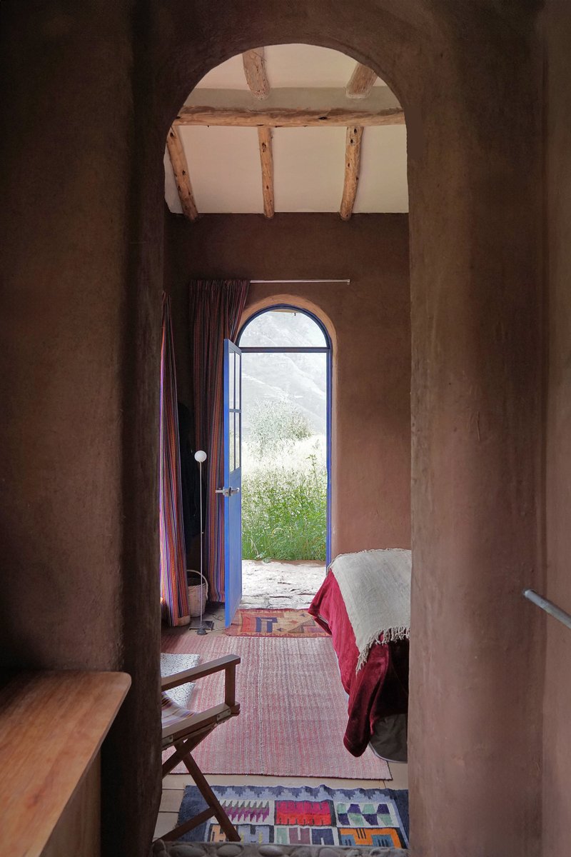 Arched doorway framing a bedroom with exposed timber ceiling beams and an open entrance to the landscape