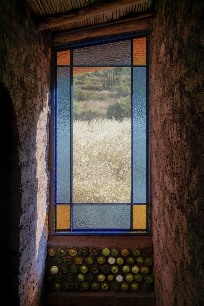 Tall window with colored glass panes and a grid of glass bottles embedded in the earthen sill