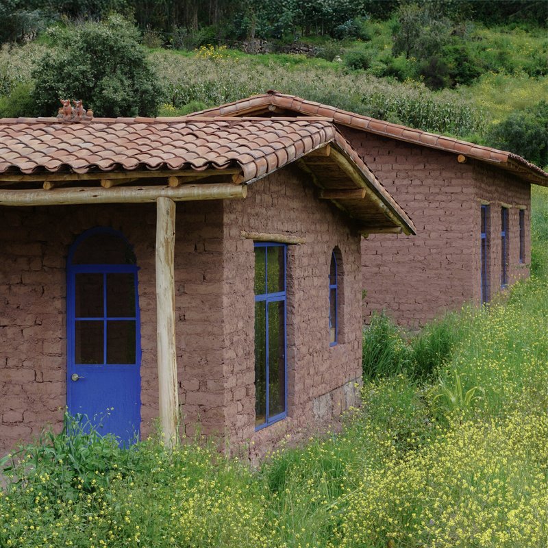 Adobe brick structure with blue painted doors and terra cotta tile roof nestled in wildflower meadow