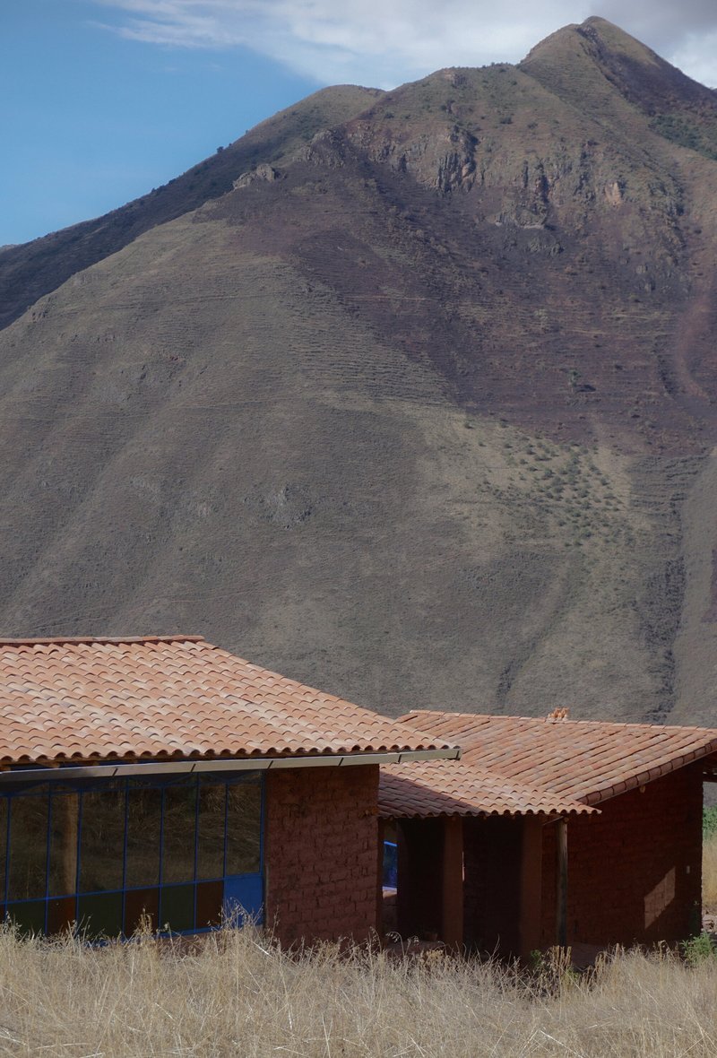 Clay tile roofs and adobe walls against a volcanic mountain slope under blue sky