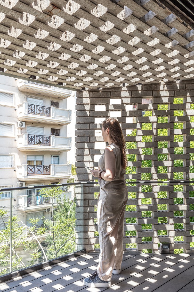 Balcony view through the perforated brick screen creating dappled shadows with a person standing inside