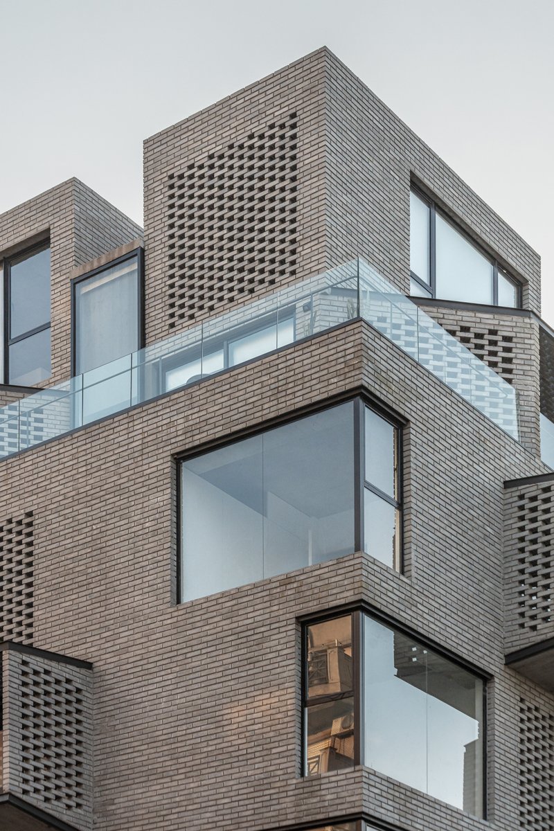 Stacked brick facade with perforated panels and large corner windows under overcast sky