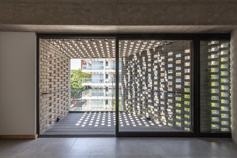 Interior view through sliding glass doors to a balcony enclosed by perforated brick screens casting dappled light