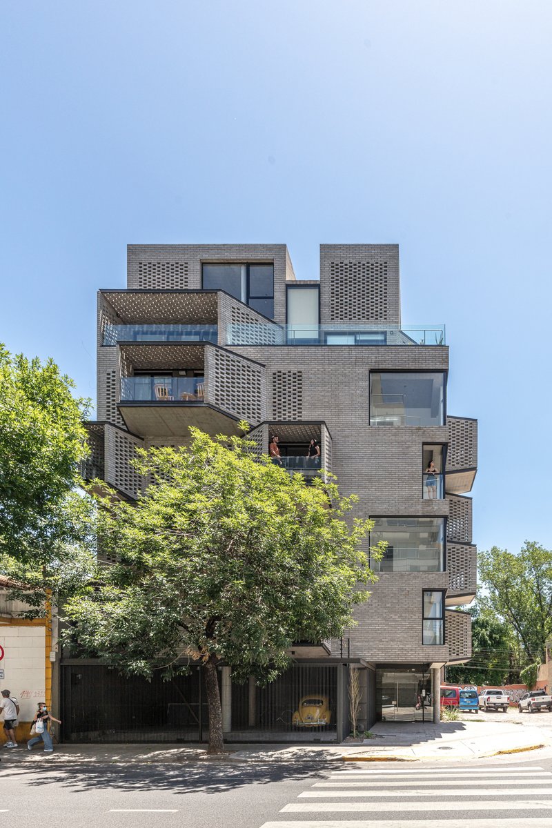 Street view of the stacked brick facade with offset balconies and perforated screens under a clear sky
