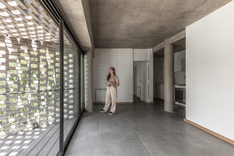 Open living space with perforated brick screen filtering daylight beside a concrete ceiling and grey tile floor