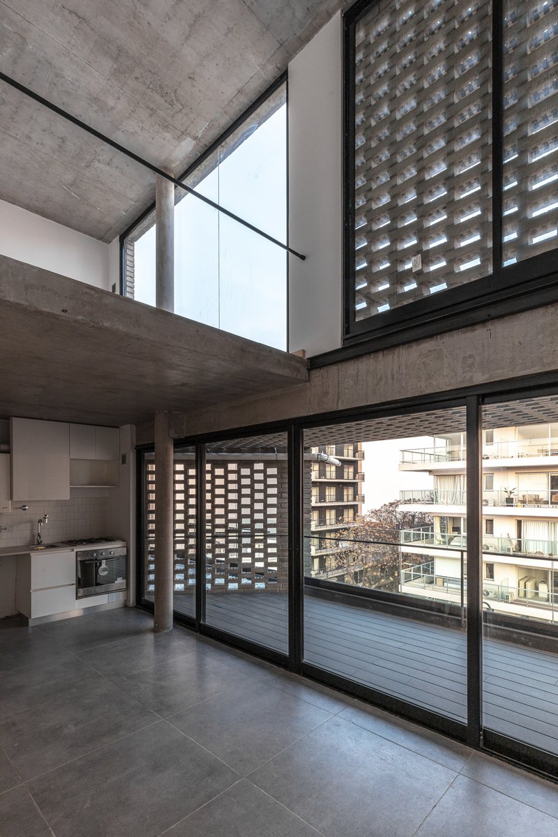 Double-height living area with mezzanine level and perforated brick screens beyond sliding glass doors