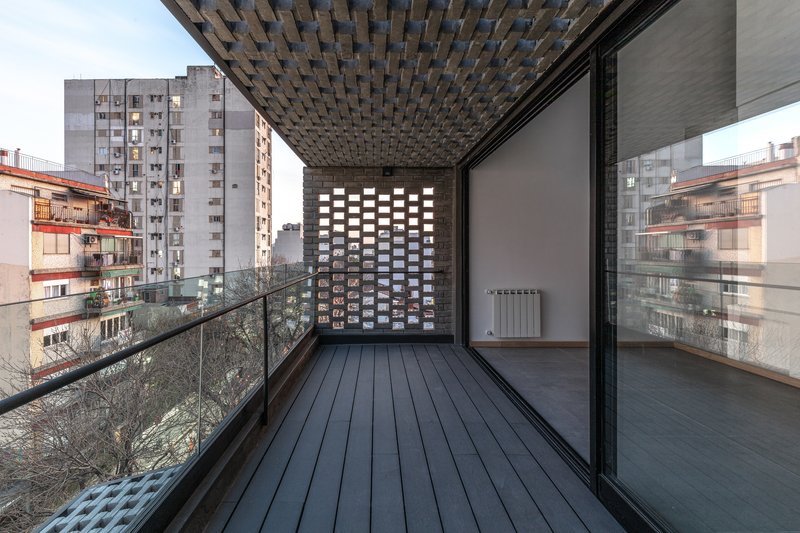Exterior terrace with dark wood decking under a patterned brick soffit and glass railing at dusk