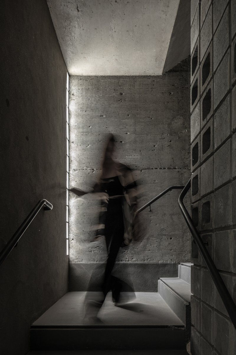 Concrete staircase landing with a figure in motion caught in daylight from a vertical slot window