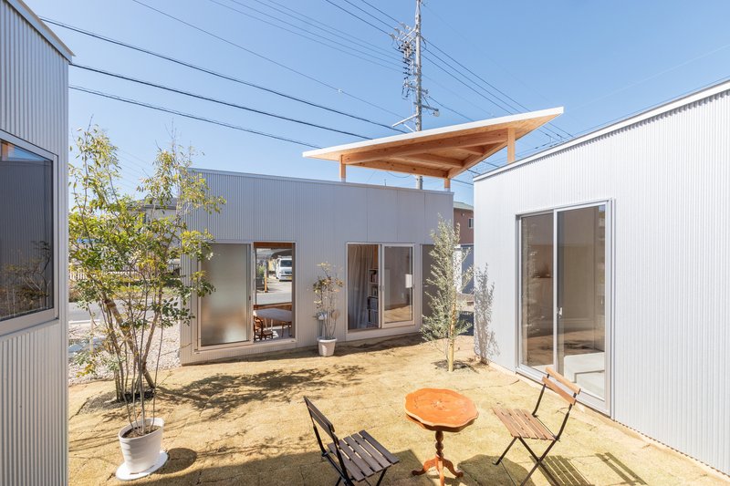 Courtyard garden with sand ground cover, planted trees, and corrugated metal-clad volumes on three sides