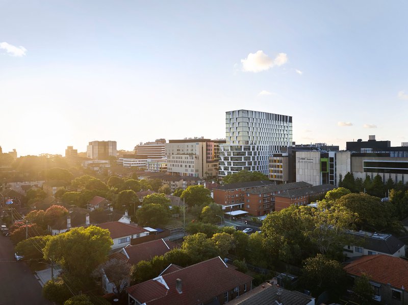 Tower with protruding floor plates visible in warm evening light across low-rise residential neighborhood