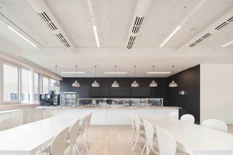 Communal kitchen with black wall-mounted cabinetry and pendant lights hung above white tables