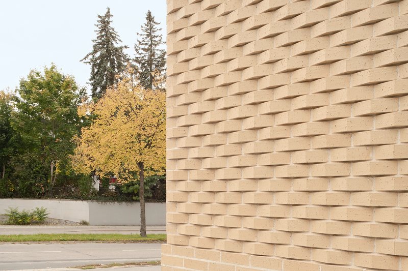 Textured brick facade with projecting headers beside a young tree in autumn leaf