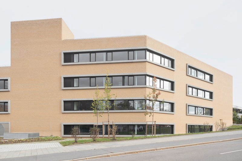 Street view of the textured brick facade with ribbon windows and recently planted saplings