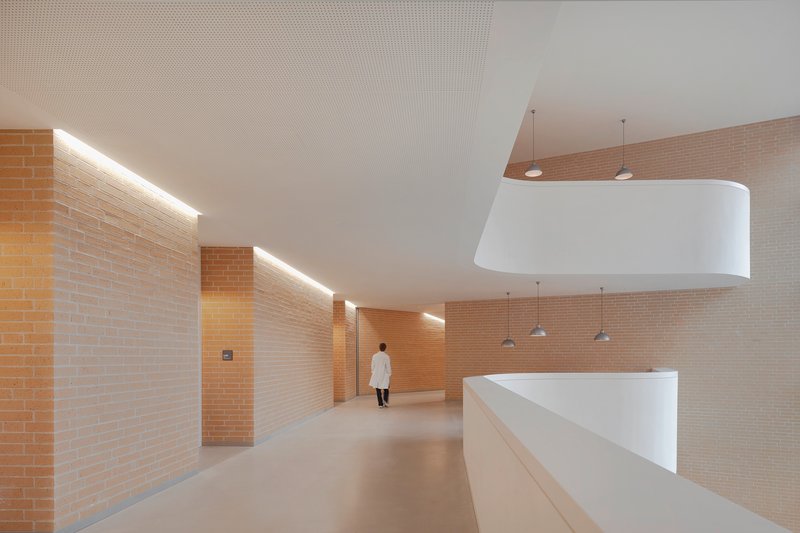 Interior corridor with yellow brick walls and linear cove lighting as a figure walks away