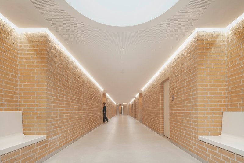 Long corridor with yellow brick walls and continuous linear cove lighting with a walking figure